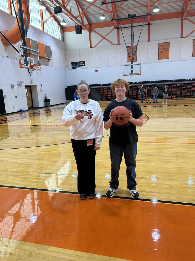 Adult in white sweatshirt and student in black t-shirt holding a basketball standing in a gym