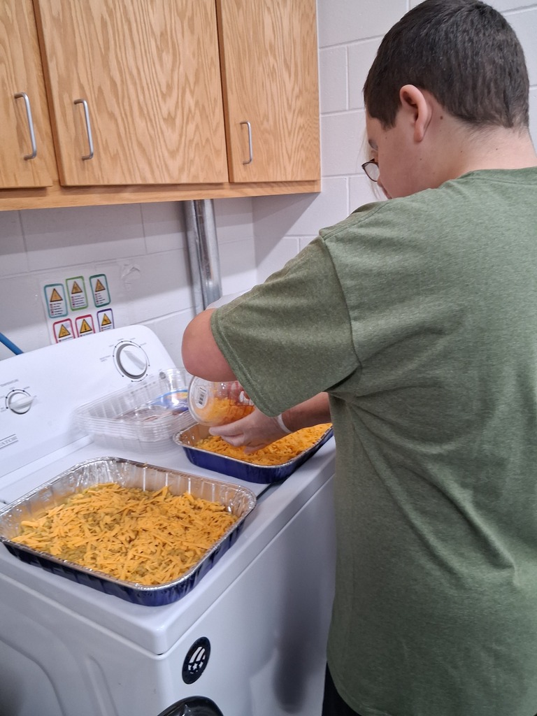 student putting cheese on top of mac and cheese dish