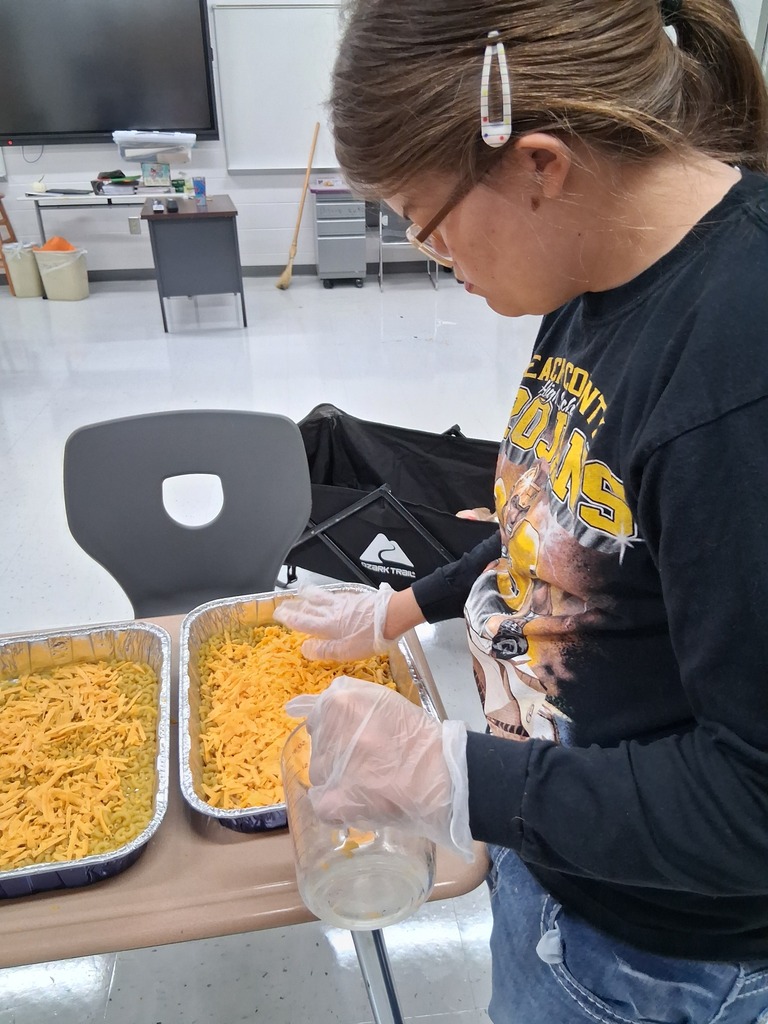 student putting cheese on top of mac and cheese dish