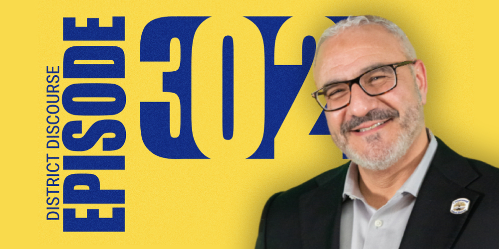 A bold promotional graphic for “District Discourse Episode 302” features a bright gold background with large dark blue text. The word “EPISODE” is written vertically along the left side in very large bold block letters, while the words “DISTRICT DISCOURSE” appear in smaller vertical dark blue text beside it. Centered prominently across the graphic is the large number “302” in oversized dark blue numbers. On the right side of the graphic is a smiling man with short gray hair, a trimmed gray beard, and black rectangular glasses. He is wearing a dark blazer over a light gray collared shirt and has a circular pin attached to his blazer lapel. The man faces slightly toward the camera and smiles warmly. The overall design uses a clean, modern podcast or interview-show style with strong school colors of blue and gold.