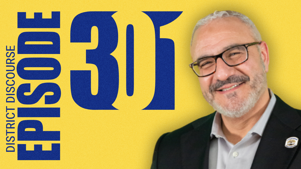 A yellow graphic promoting “District Discourse Episode 301.” Large blue text reads “EPISODE 301” with “District Discourse” written vertically along the left side. On the right side is a portrait of a smiling man with short gray hair, glasses, and a trimmed beard, wearing a dark blazer over a light-colored shirt with a small lapel pin. The background is a textured yellow gradient.