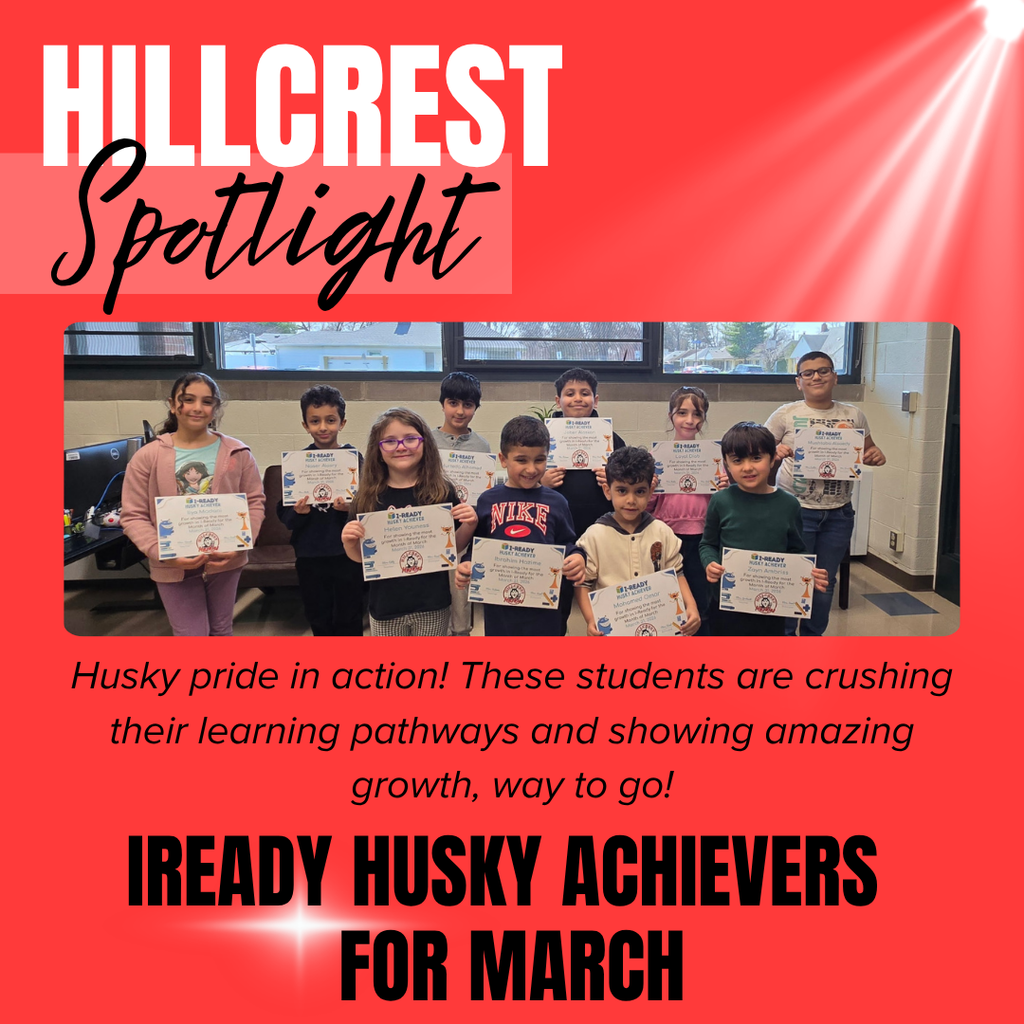 A bright red graphic with a spotlight effect shining from the top right corner and large white text at the top that reads “HILLCREST,” with the word “Spotlight” written in black cursive script overlapping it. In the center of the image is a group photo of ten elementary-aged students standing in a classroom in front of windows, each holding a certificate. The certificates appear to say “i-READY HUSKY ACHIEVER” with additional smaller text and graphics, though the smaller details are not fully legible. The students are smiling and standing in two rows, wearing casual clothing such as hoodies and T-shirts, and appear proud of their accomplishments.