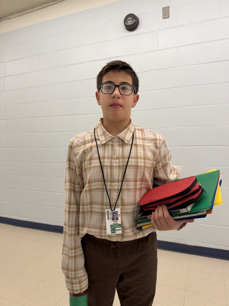 A boy wearing glasses and a plaid shirt holds a stack of colored folders.