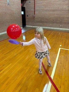 Girl holding a paddle hitting a balloon. 