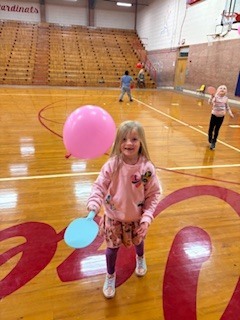 Girl holding a paddle hitting a balloon. 