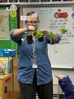A teacher holding up a plant. 