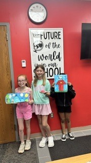 Three students holding their art projects.  