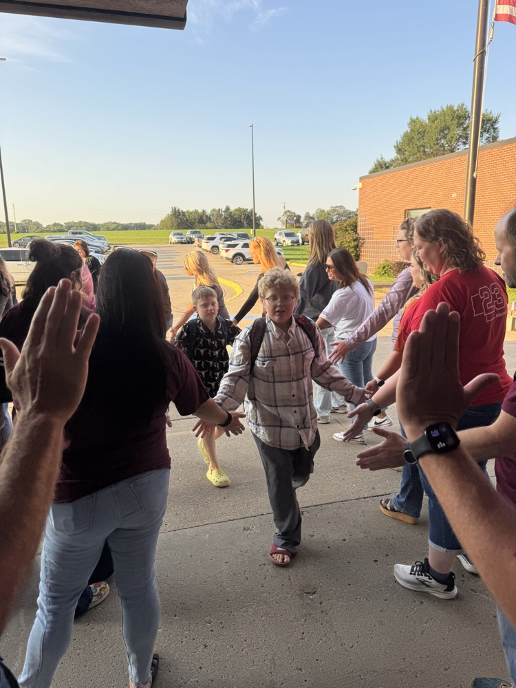 Members of Crofton Community Schools are smiling in front of the high school to greet and high five the students