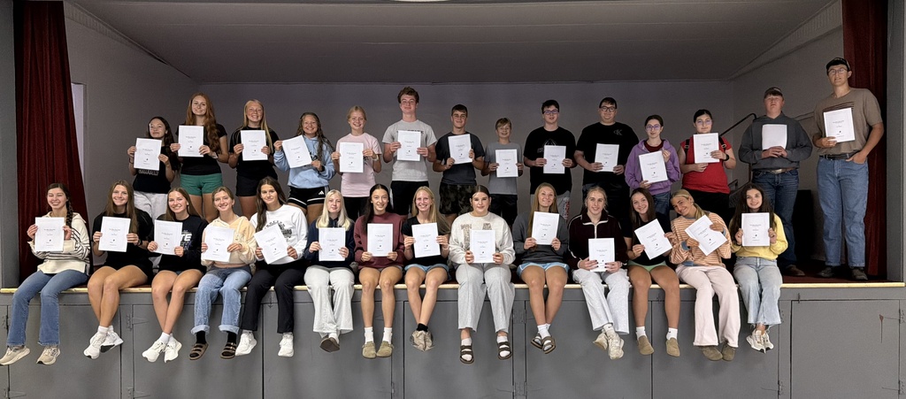 Students sitting on stage holding scripts