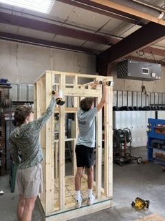 Construction Trade students fastening their door opening wall to the rest of their structure. 