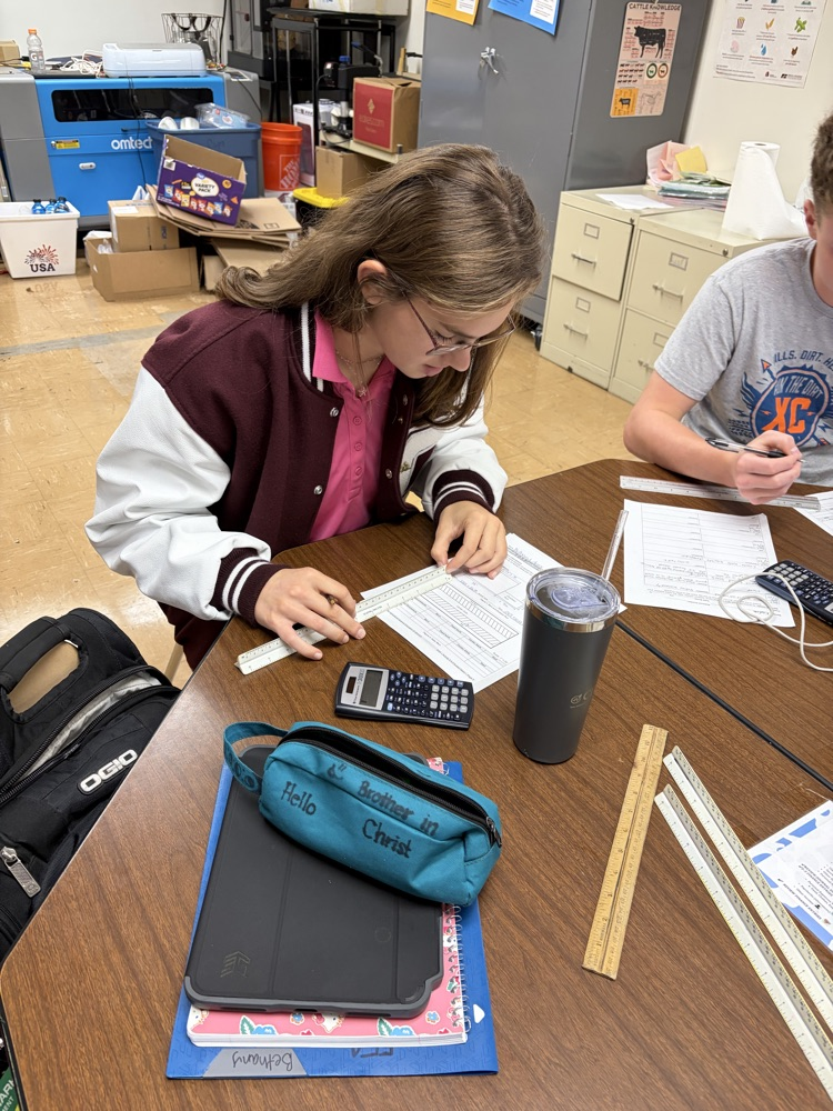Student calculating facility size using scale measurements.