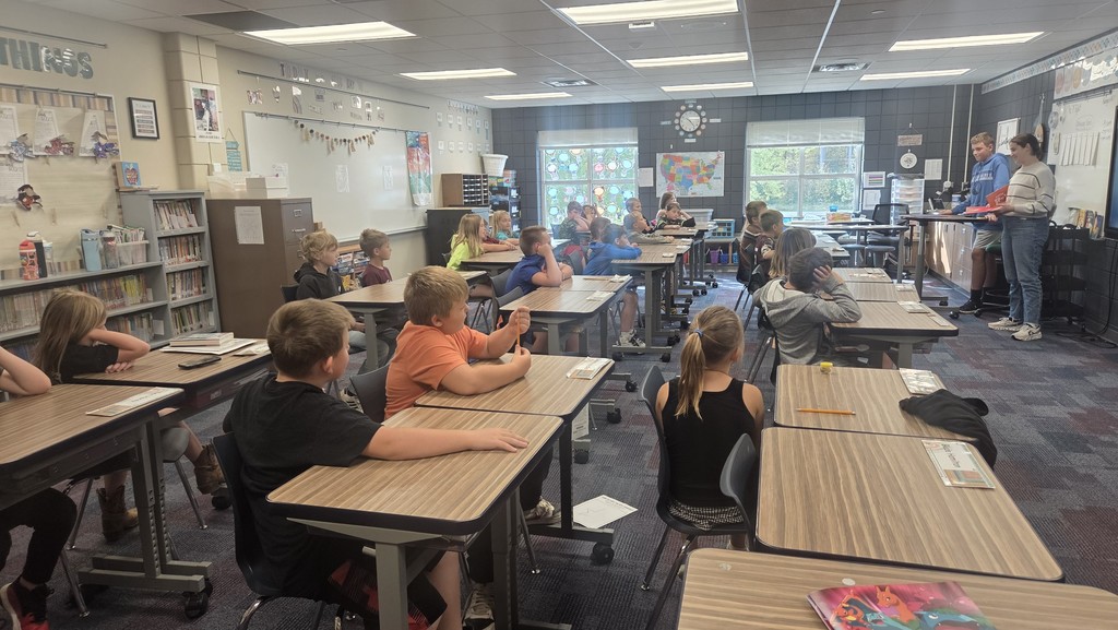 two high school students in front of a classroom of students in their desks