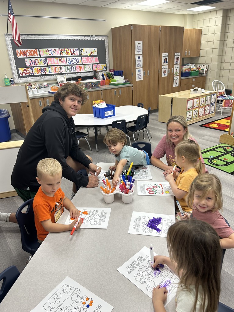 high school student kneeling down working with younger students and a para at a table