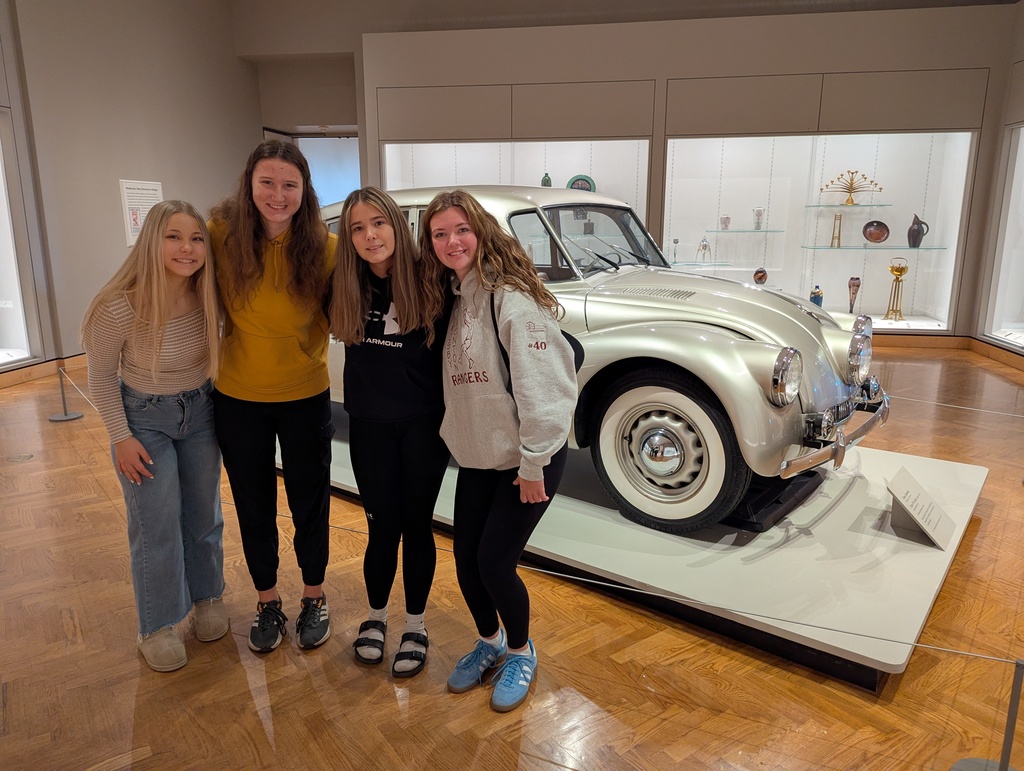 Four female students posing in front of a model car at the art institute