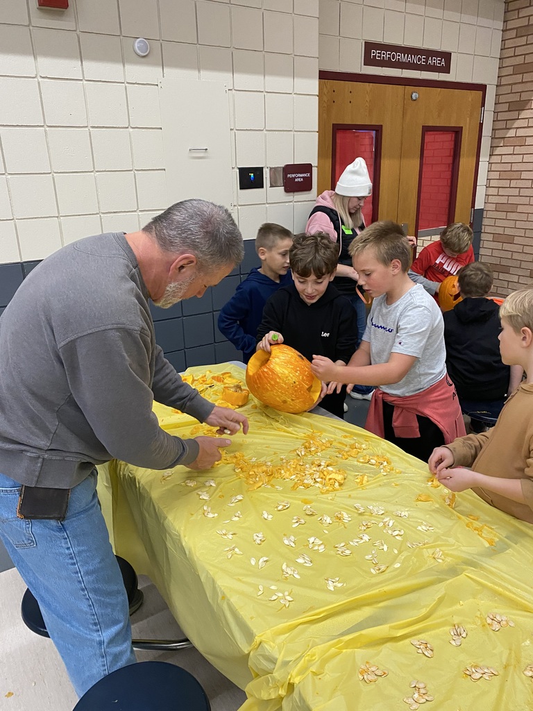 two students and an adult helper are gutting a pumpkin and carving it and counting seeds