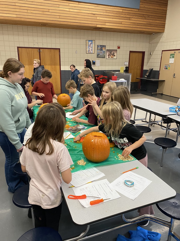3rd graders and a senior gather around a pumpkin that is being carved