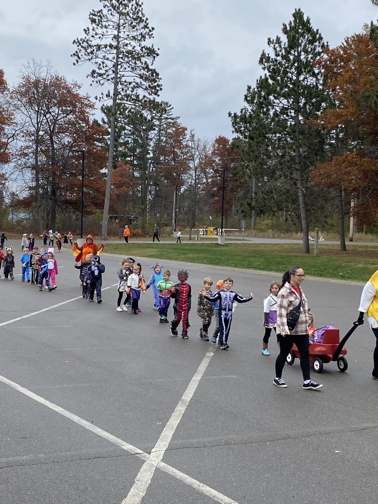 Kindergarten students walking in a line around the bus loop in their Halloween costumes