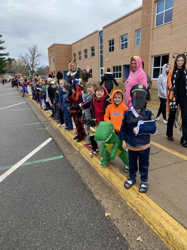 Students and teachers wearing their Halloween costumes standing on the sidewalk waiting for the parade to walk by