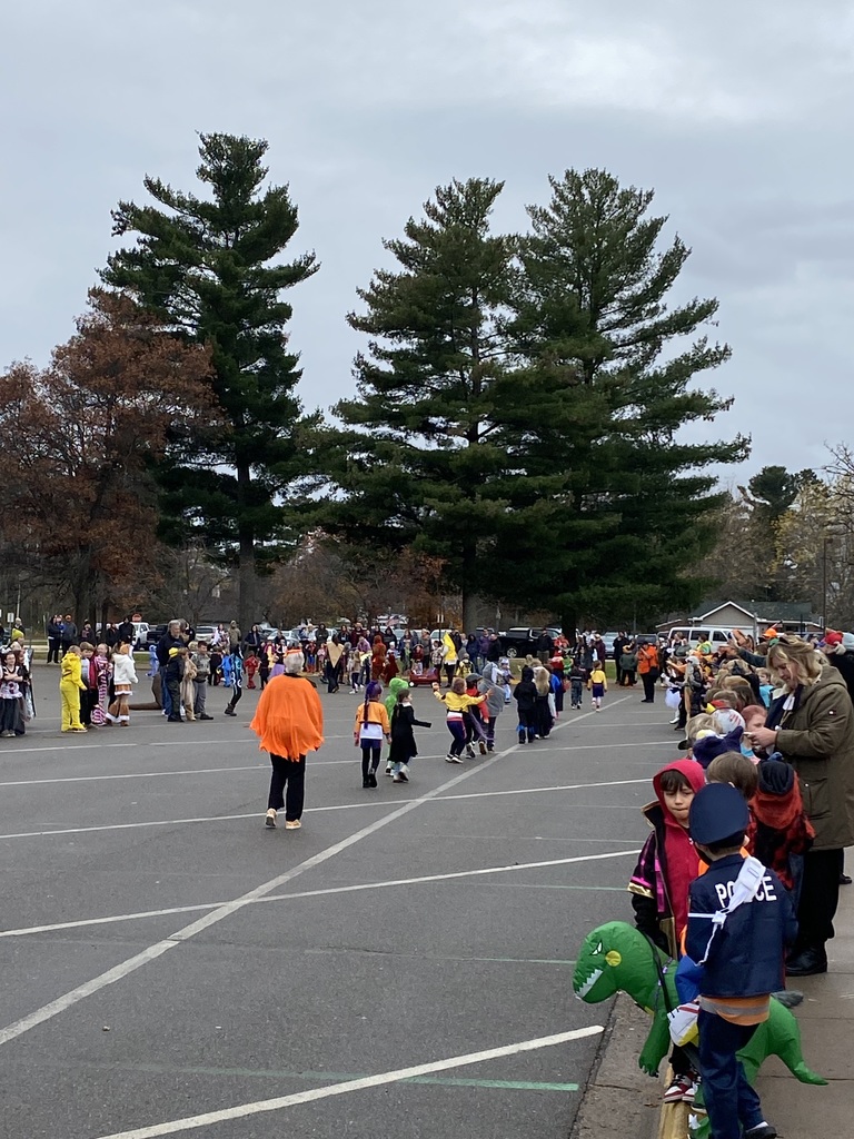 Students walking, students lined up on the sidewalk watching them parade around in their Halloween costumes