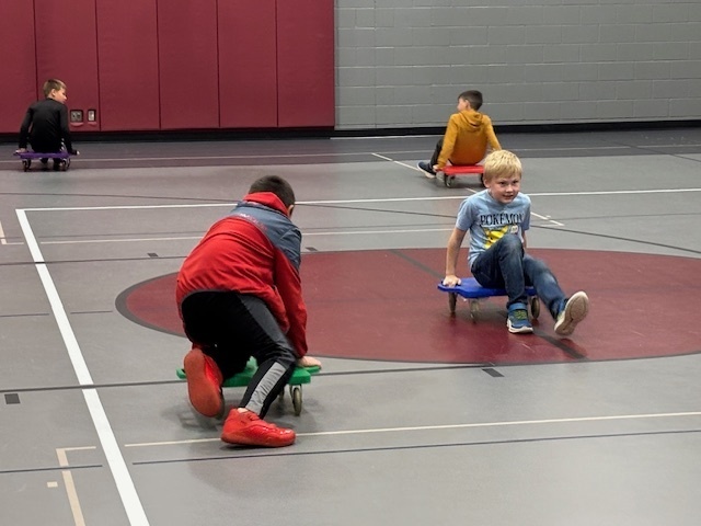three students riding scooters in the gym during Fall Into Reading Night at CRES