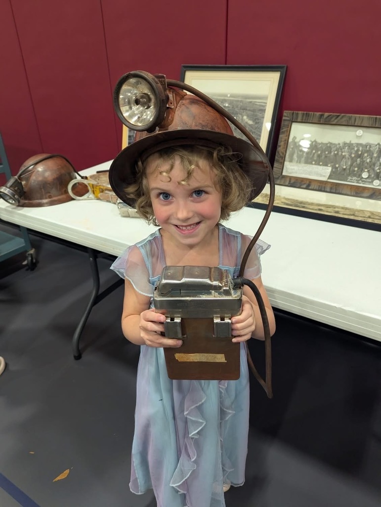 A young female student holding an old mining light that is on her mining hat