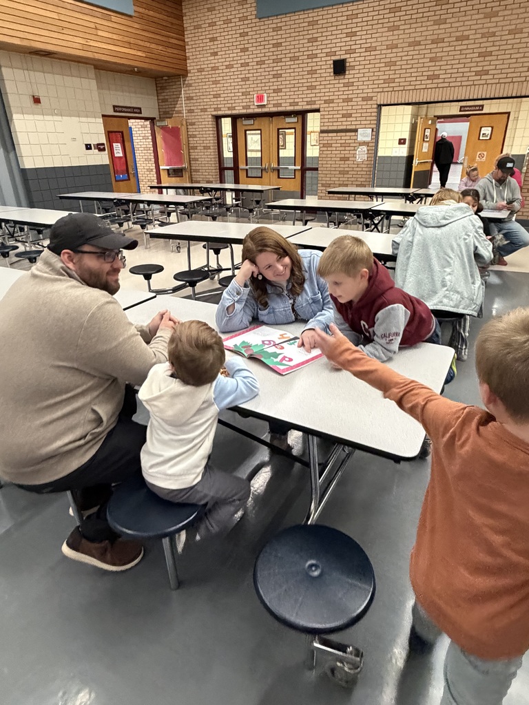 Two students sitting at the cafeteria table with their mom and dad while reading a book