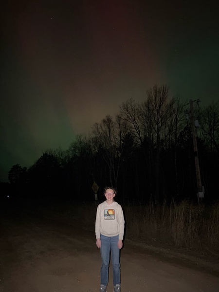 s student standing on the road with the northern lights shining in the sky above