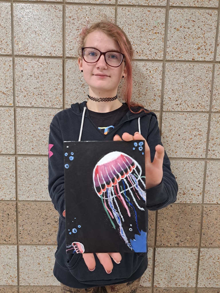 Student holding her painting of a colorful jellfish on a black background 
