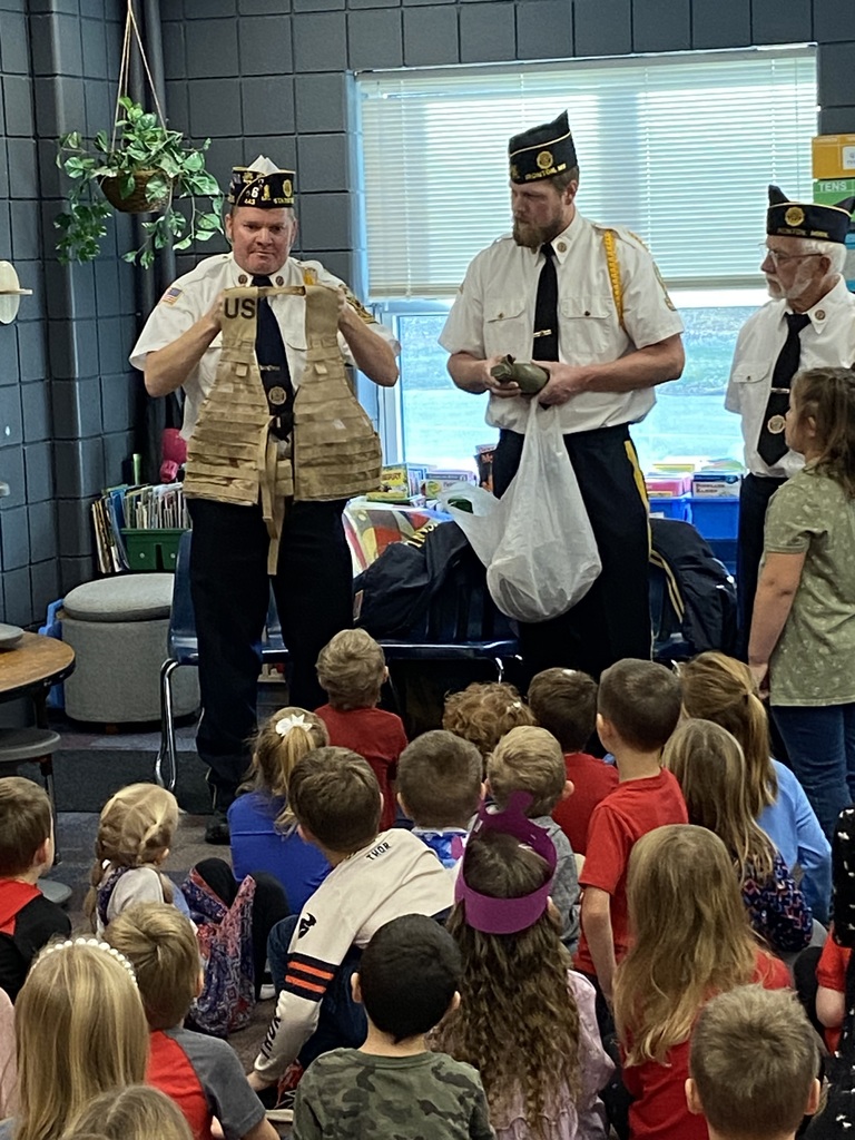 kindergarteners sitting on the floor as they look at our local veteran showing his military vest to them and telling stories