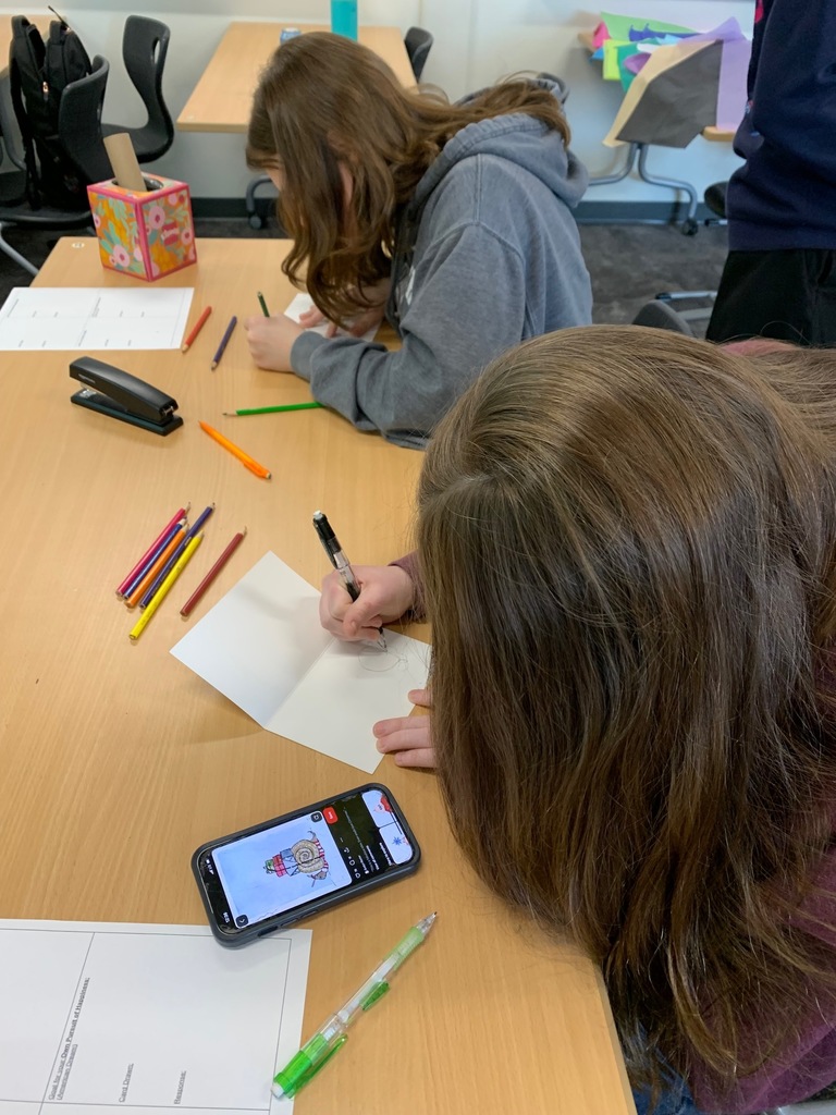 two students writing out their holiday cards for Holiday for heroes. 