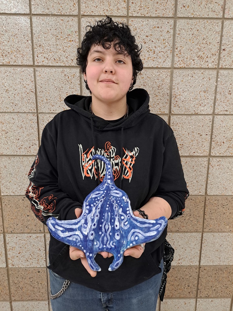 Student holding a blue and white clay sculpture of a mantaray