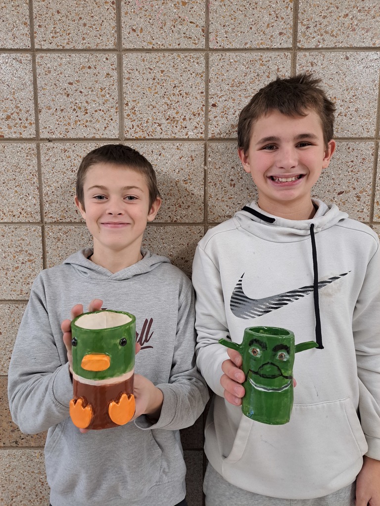 Two 7th grade boys holding a clay mug, one of a dug and the other Shrek