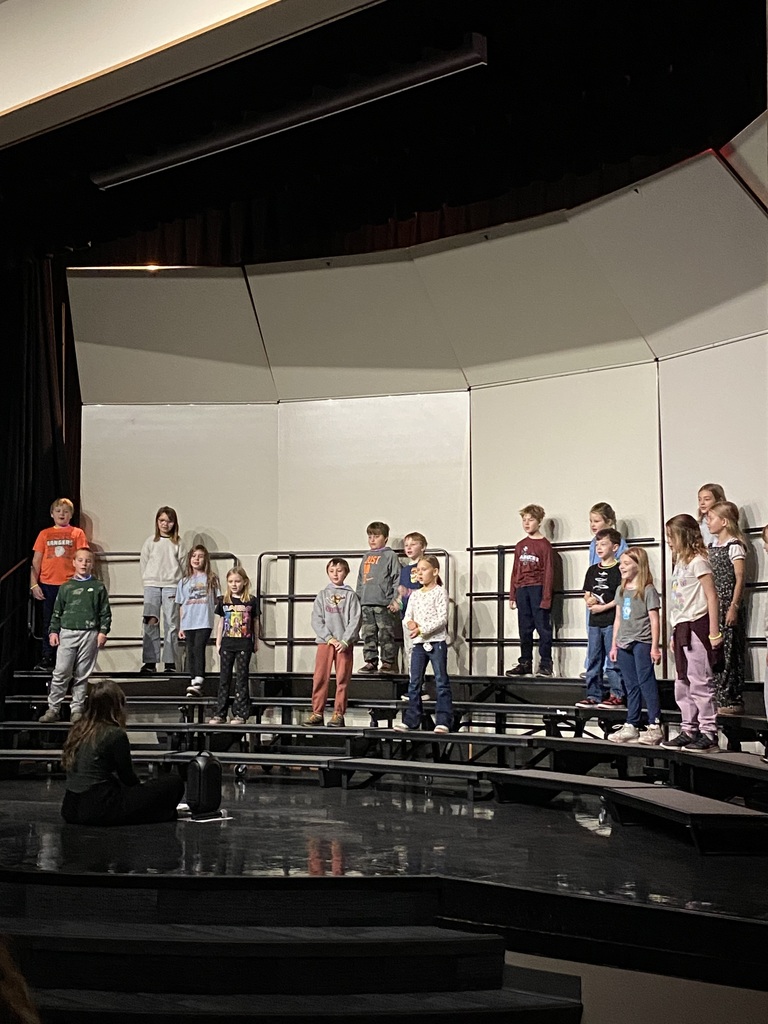 3rd graders standing on the risers in the performance area singing a song at their expo