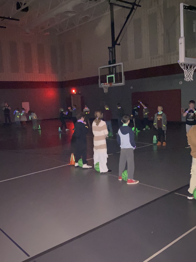 third graders lined up standing on a line across from one another with green basketballs and glow bracelets and necklaces with the lights off at their expo