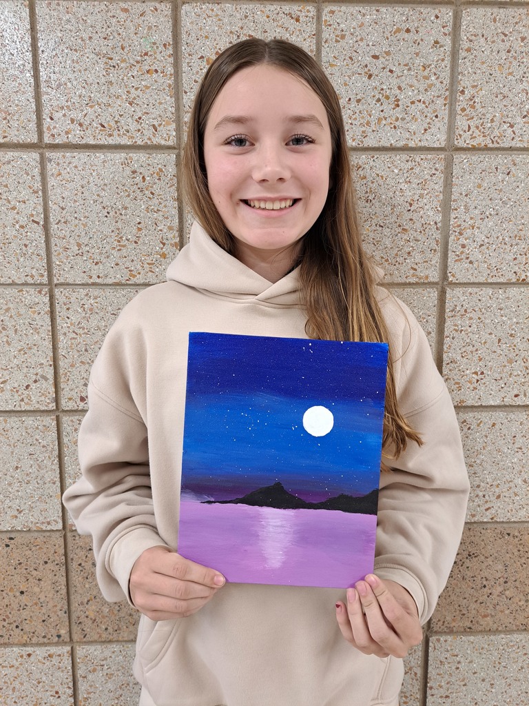 Female student holding an acrylic painting of a dark blue sky with stars and the moon shingin bright leaving a reflection into the light purple water below