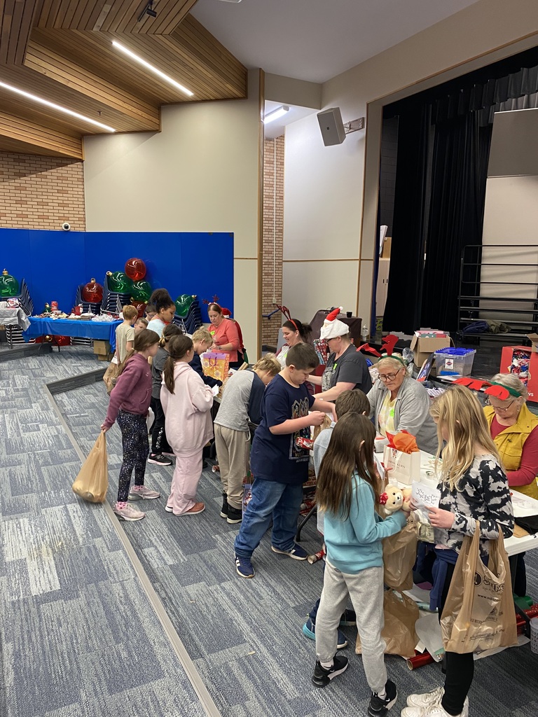multiple students standing at tables in front of adults who are wrapping their gifts from Jingle Bell Lane