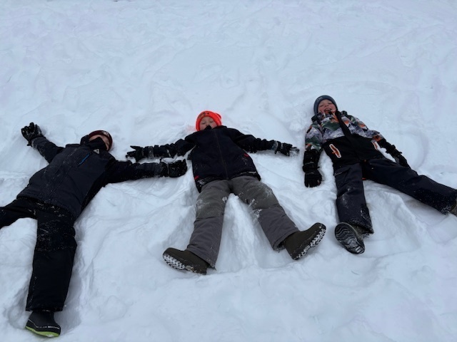 three students laying in the snow making snow angels