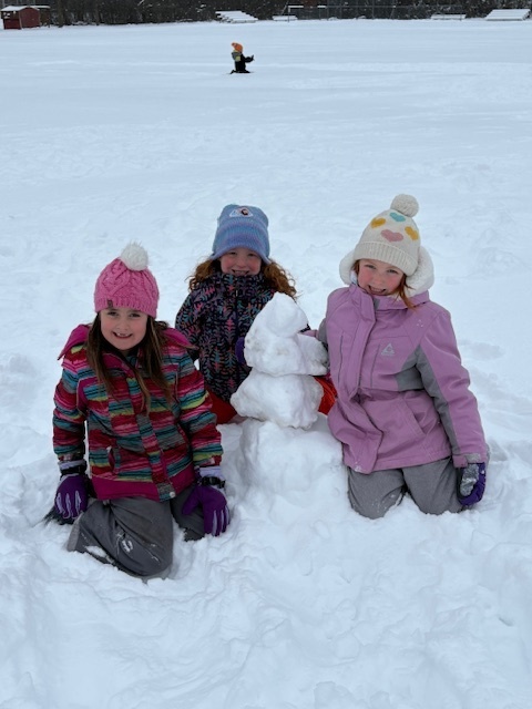 three female student sitting next to a snowman that they built