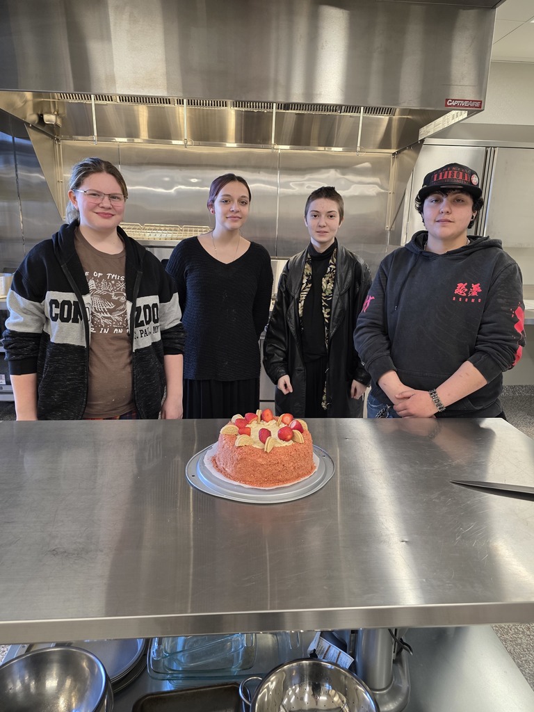a mix of female and male student posing in their kitchen behind their strawberry cake they made in culinary class