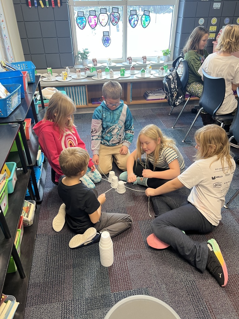 5 third graders sitting on the floor working together using a string to stack styrofoam cups to build a christmas tree using only a string