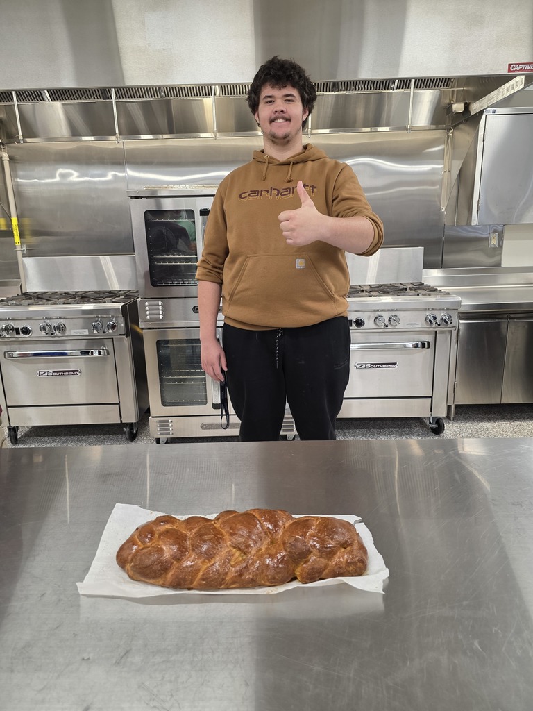 male student giving a thumb up for his loaf of challah bread on a sheet of parchment paper