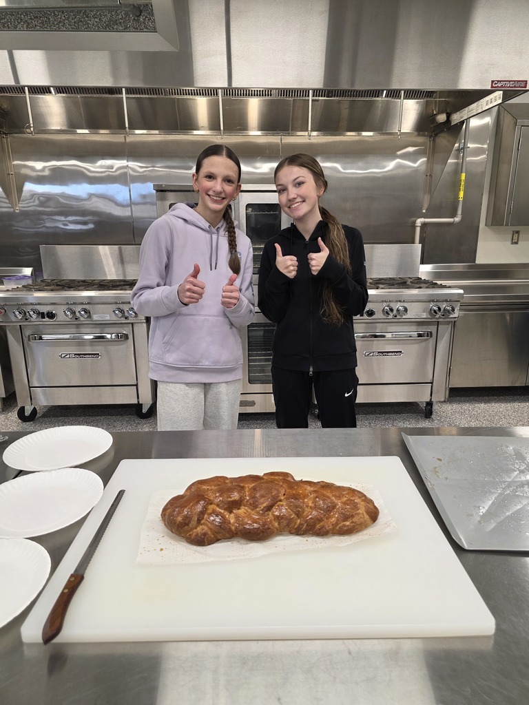 two female students giving two thumbs up for their loaf of challah bread on the cutting board