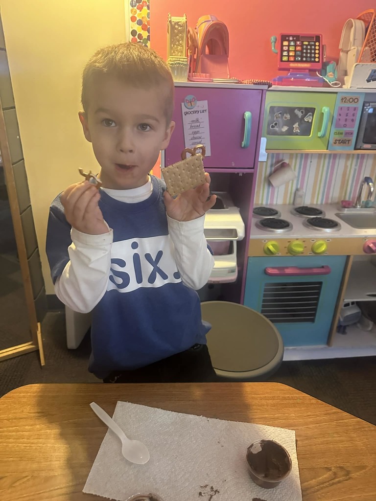 male kindergarten student holding a graham cracker with pretzels stuck to it