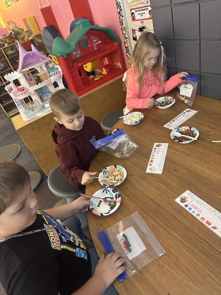 male and a female student putting animal crackers, pretzels and m&ms into a baggie for a snack
