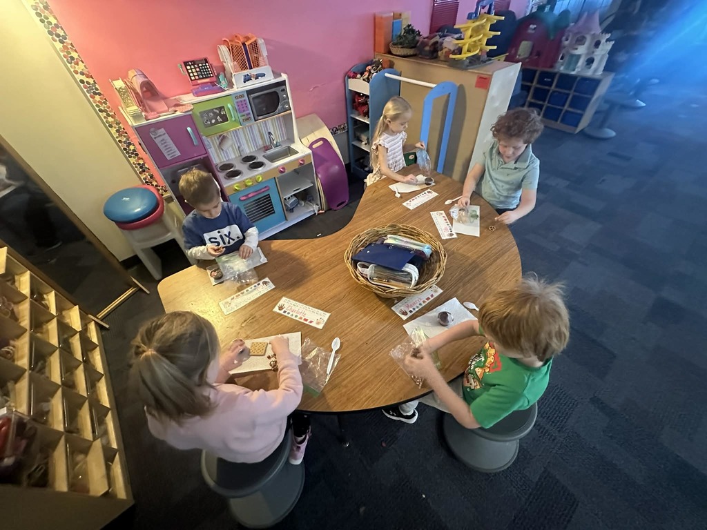 5 kindergartners making reindeer out of a graham crackers frosting and pretzels