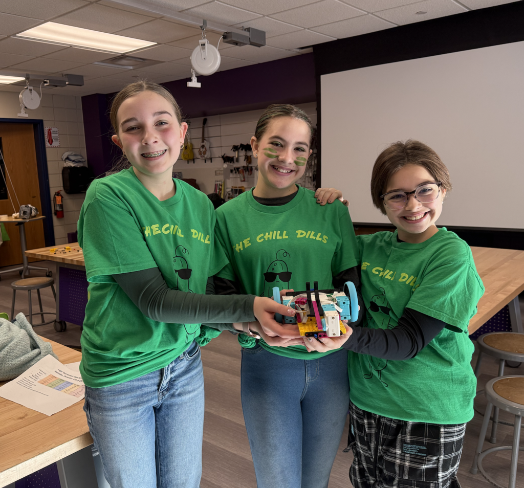Three female lego league members wearing green shirts called the Chill Dills holding their lego creations