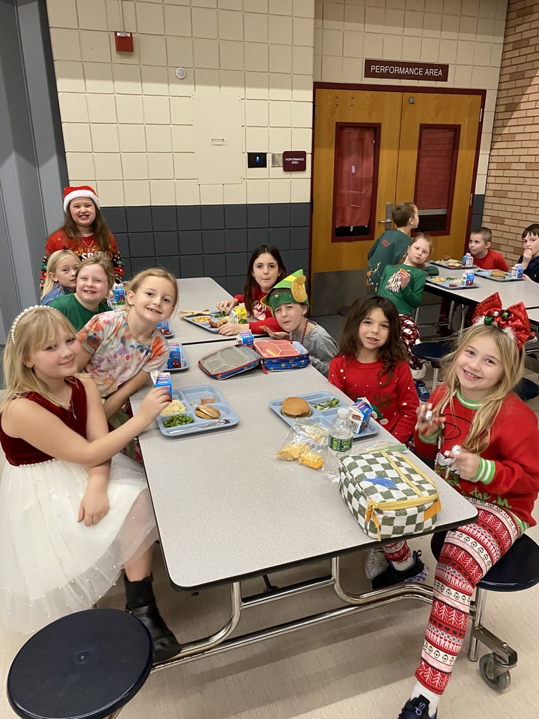 9 students having lunch dressed in holiday dresses and hoiday shirts and pants ready for winter break