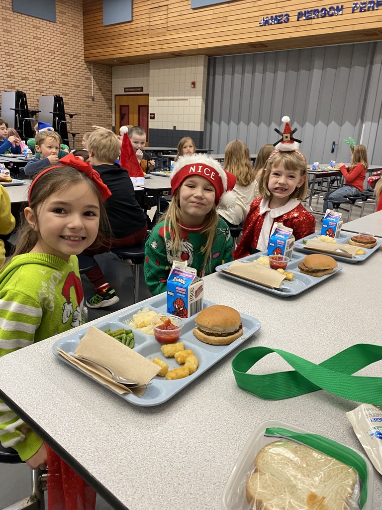 three female students having lunch one wearing a grinch sweater, one with a santa hat that says NICE and the other with a santa headband on