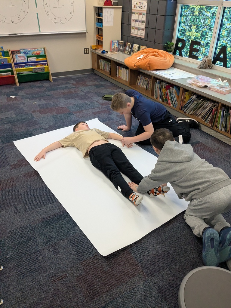 two male students tracing another male student who is laying on a big sheet of white paper