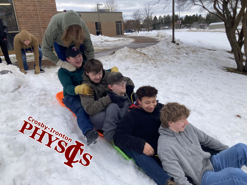 6 male students on two different sleds making a train going sledding down a hill